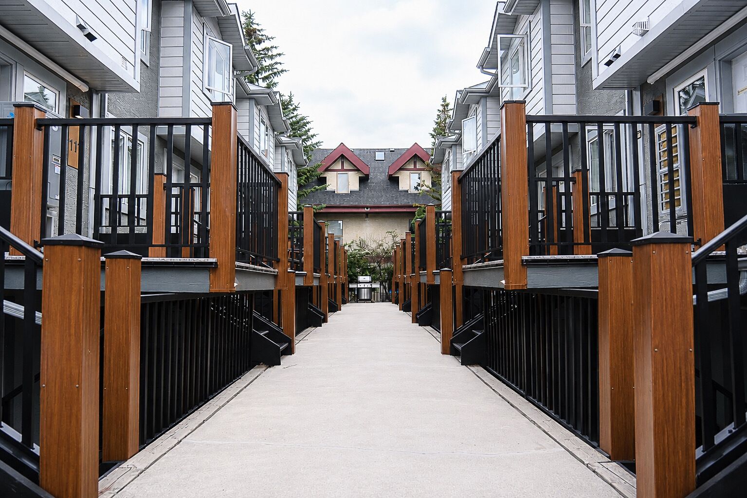 A corridor with a central walkway flanked by buildings with wooden railings and black metal gates.
