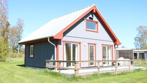 A two-story building with a red and grey exterior, large windows, and a wooden deck in front. - Beautiful home in Löttorp with WiFi (Löttorp)