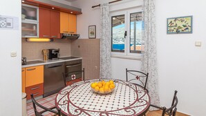A compact kitchen with orange cabinets, a coffee machine, and a dining area with a mosaic table and a bowl of lemons.