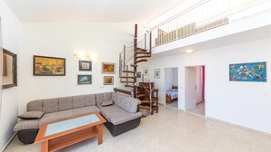 A spacious living area with a large sectional sofa, a wooden coffee table, and a spiral staircase leading to an upper floor.