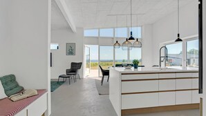 A modern kitchen with a large island, a dining area with a view, and a cozy seating area with a book and pillows.