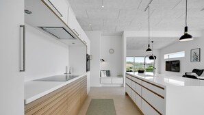A modern kitchen with white cabinetry, a wooden countertop, and a built-in stove. There is a window providing a view of the outdoors.