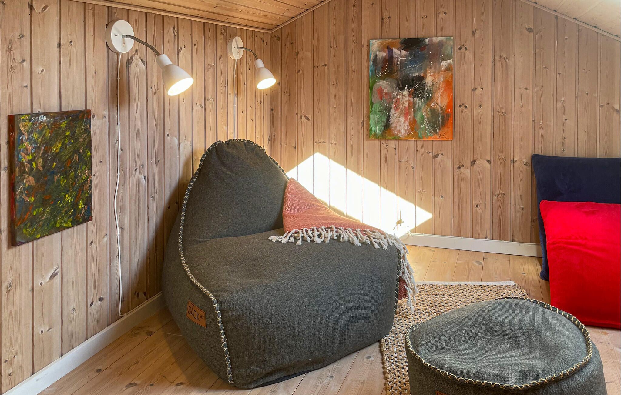 A cozy room with wooden walls, a bean bag chair, a small ottoman, and a red cushion.