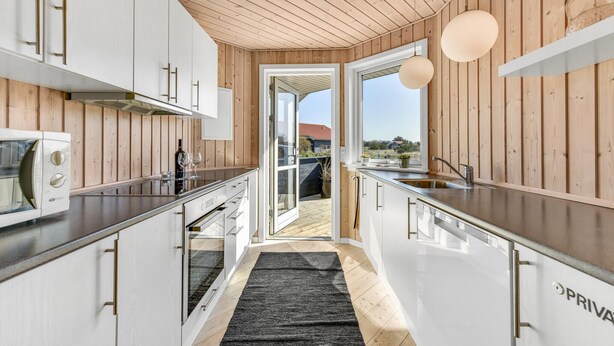 Une cuisine moderne avec un lambris en bois, des appareils électroménagers en acier inoxydable et une vue sur l’extérieur.