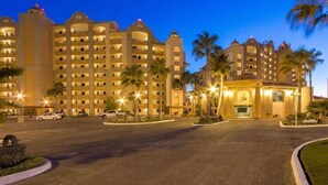 A multi-story hotel with a central courtyard, palm trees, and a well-lit entrance.