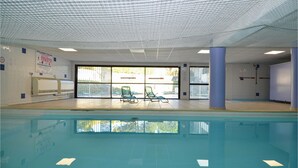 Una piscina interna con pareti in vetro trasparente, pavimento piastrellato e diverse poltrone relax.
