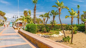 Un paseo marítimo frente a la playa con palmeras, un camino empedrado y una playa al fondo.