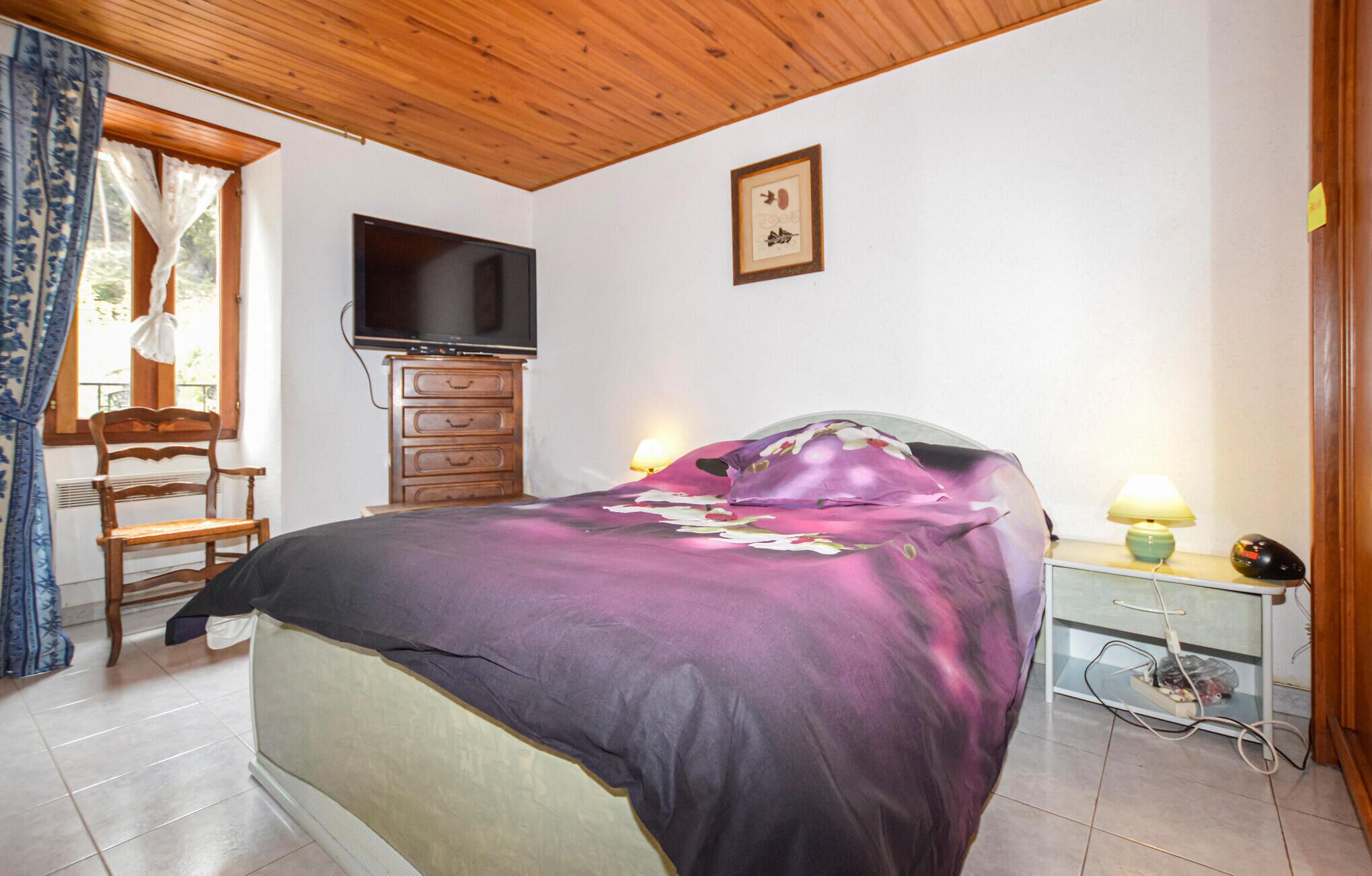 Quarto com cama, penteadeira de madeira, televisão e uma mesinha com luminária.