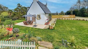 A white house with a sloped roof, a patio with a table and chairs, and a garden with a wooden fence. - 2 bedroom nice home in Pleuven (Pleuven)