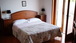 A bedroom with a wooden headboard, a floral bedspread, two bedside tables with lamps, and a sliding glass door leading to an outdoor area. - Holiday flower villa with pool (Misterbianco)