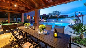 An outdoor pool area with a wooden deck, poolside chairs, and a table with a lantern. - Beautiful home in Zaton (Zaton)