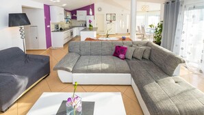 A modern living room with a grey sectional sofa, a black armchair, and a glass coffee table with a vase of flowers. - Beautiful home in Zaton (Zaton)