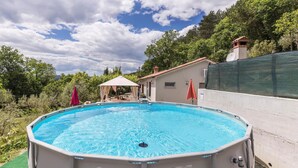 An outdoor swimming pool with a covered seating area, surrounded by trees and a hillside. - Pet friendly home in Kostrcani with WiFi (Kostrcani)