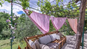 A wooden bench with cushions and a hanging pink cloth structure in a garden setting. - Pet friendly home in Kostrcani with WiFi (Kostrcani)