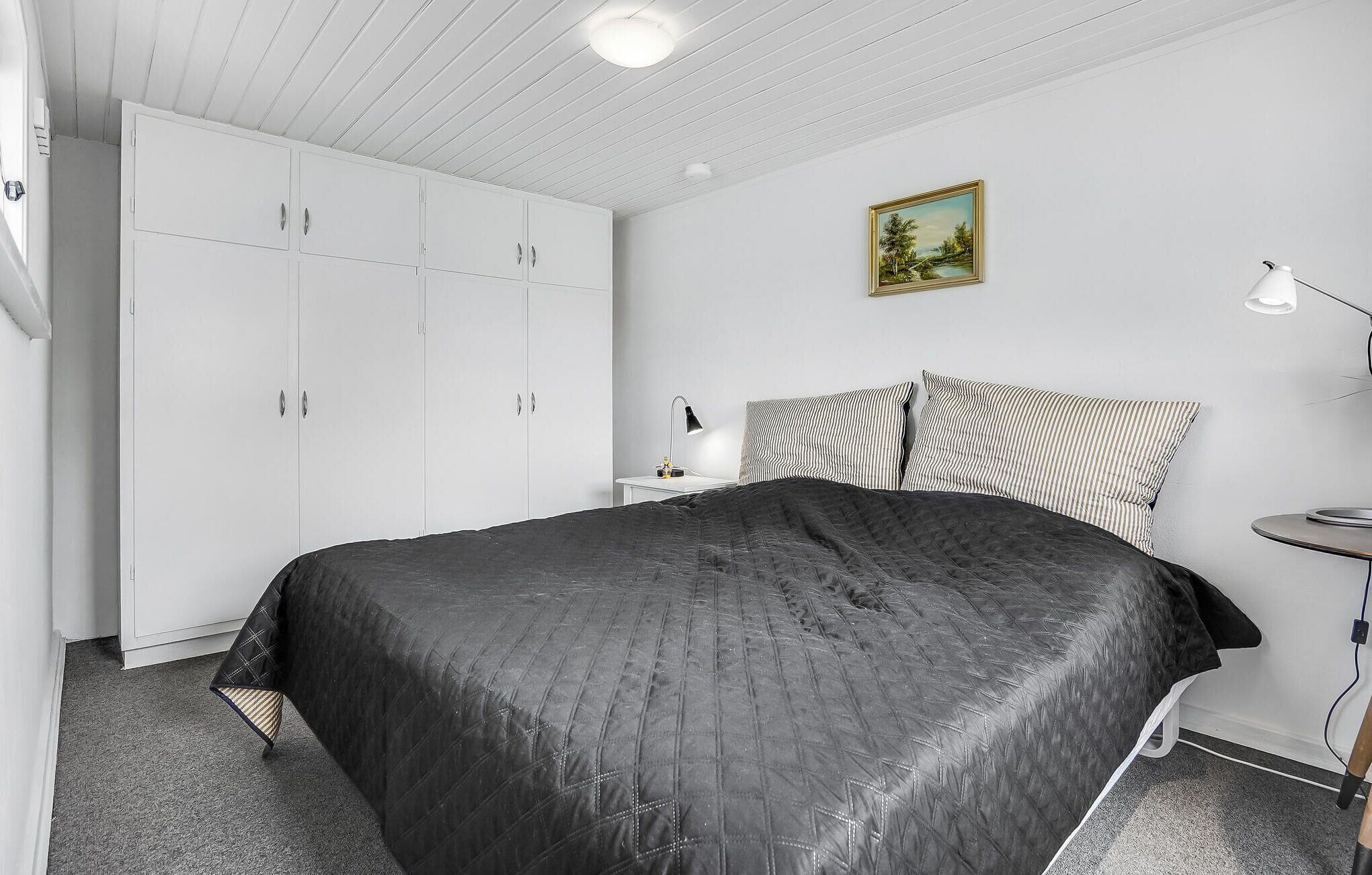 Une chambre à coucher avec un lit, une table de chevet, une lampe, une armoire et un tableau au mur.