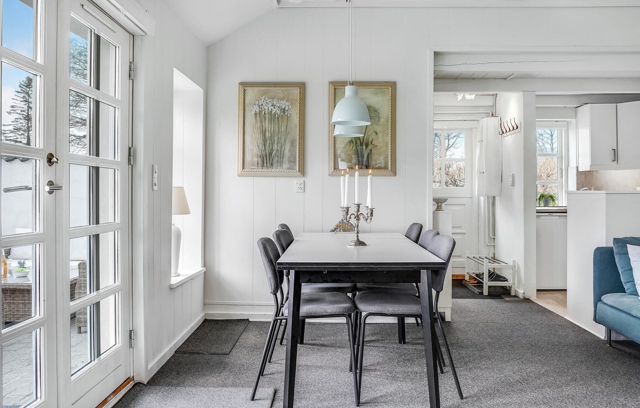 Een eetgedeelte met een tafel en stoelen, een witte deur met glaspanelen, en twee ingelijste kunstwerken aan de muur.