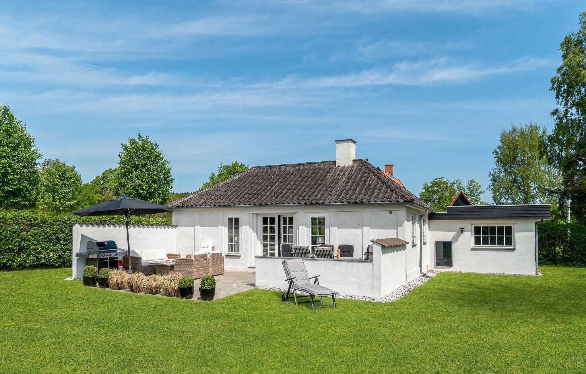 A white house with a tiled roof, a patio with outdoor furniture, and a lawn.