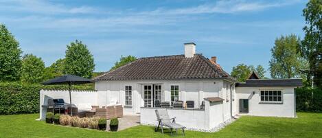 A white house with a tiled roof, a patio with outdoor furniture, and a lawn.