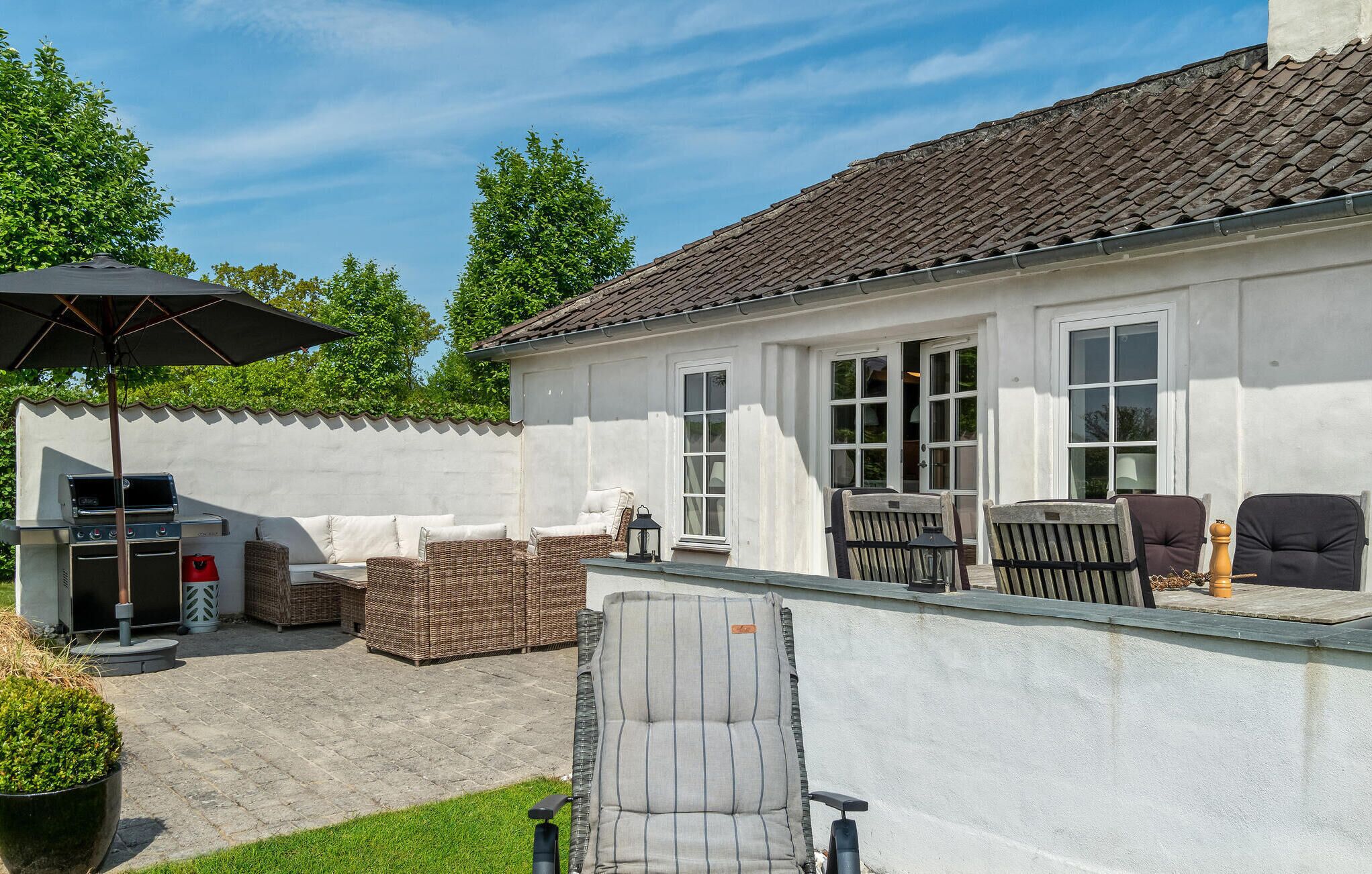 Un patio con mobiliario exterior, una parrilla y un gran paraguas.