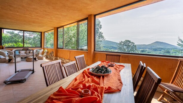 A dining area with a table set for two, a treadmill, wicker chairs, and a view of a mountainous landscape through large windows. - Nice home in Bassano Romano with WiFi (Bassano Romano)