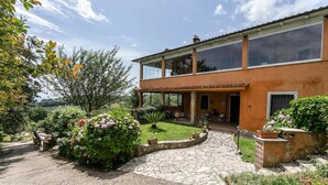A two-story house with a stone pathway leading to the entrance, surrounded by lush greenery and flowering plants. - Nice home in Bassano Romano with WiFi (Bassano Romano)