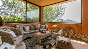 A sunlit room with wicker furniture, large windows, and a view of trees and hills. - Nice home in Bassano Romano with WiFi (Bassano Romano)