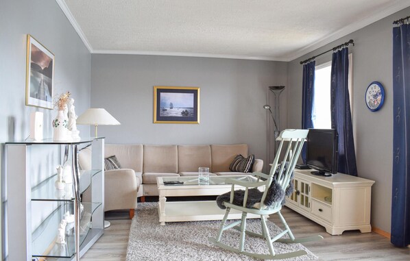 A living room with a sofa, a glass coffee table, a rocking chair, a television, and a cabinet.