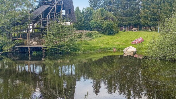 A rustic cabin with a wooden deck and a pond in front.