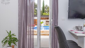 A room with a sliding glass door to a pool area, a television mounted on the wall, and a desk with a chair.