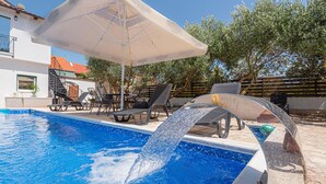 A swimming pool with a water feature, lounge chairs, and a covered seating area.