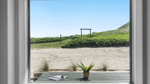 A view through a window of a sandy beach area with a wooden deck, a small table, and a potted plant. - Nice apartment in Ulfborg with WiFi (Ulfborg)