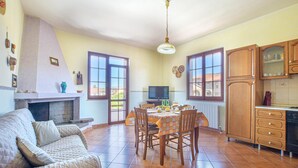 Un accogliente soggiorno con camino, una zona pranzo con tavolo e sedie, e una cucina con pensili in legno e frigorifero.