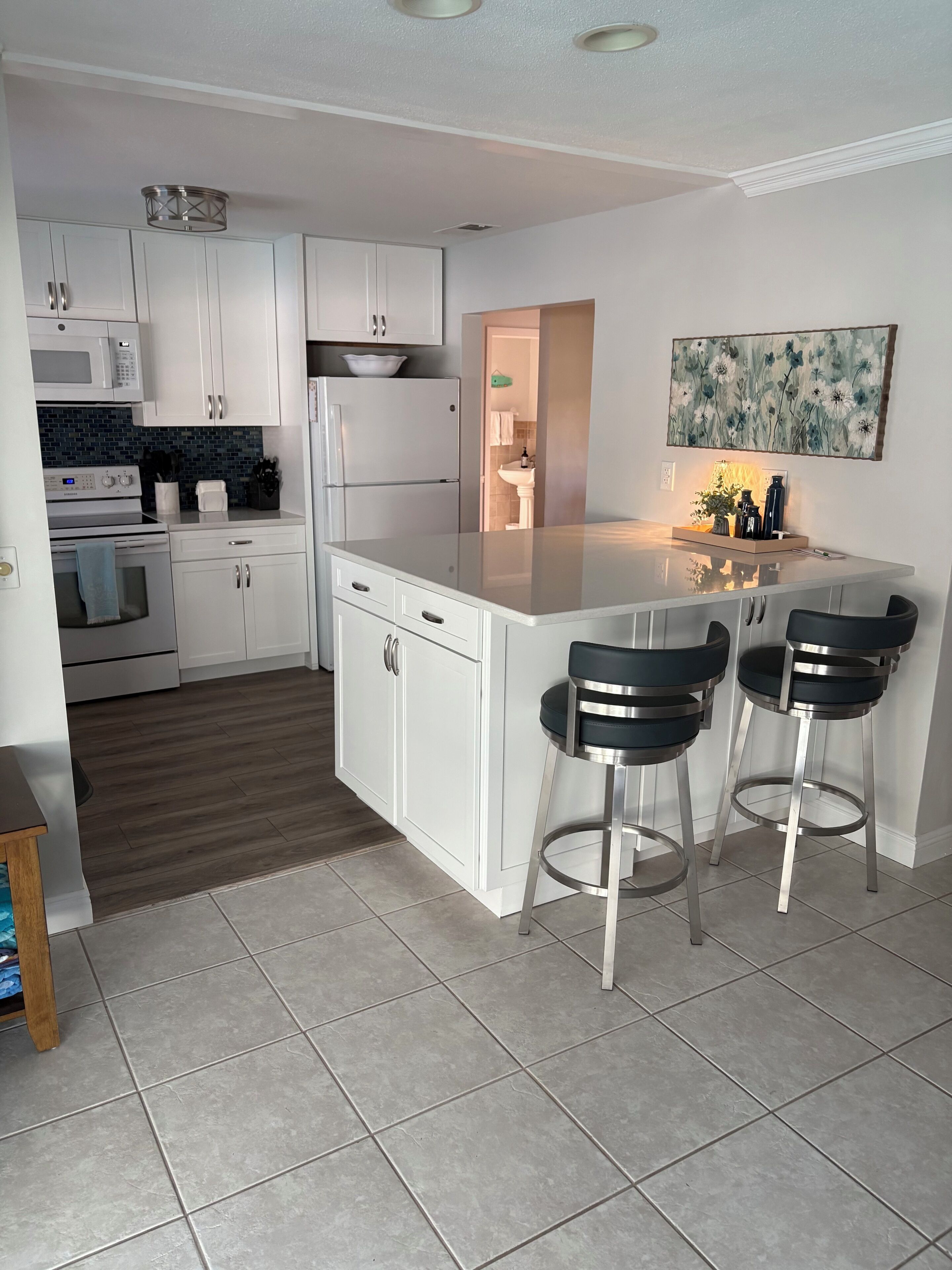 A modern kitchen with white cabinets, a central island with bar stools, a microwave, oven, and a refrigerator.