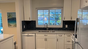 Una cocina con armarios blancos, salpicadero negro, ventana con vistas y una lámpara moderna.