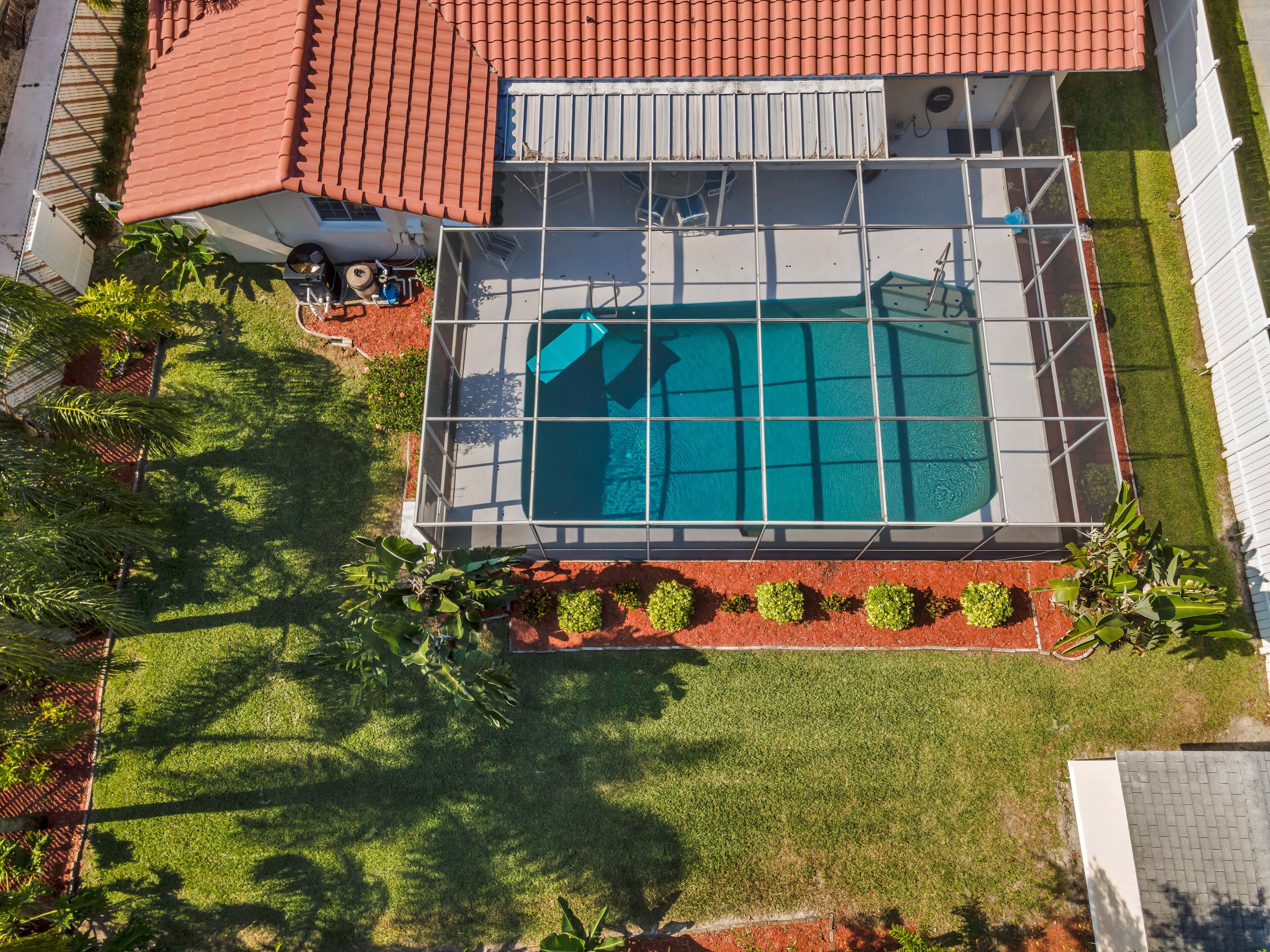 Vue aérienne d’une propriété résidentielle dotée d’une piscine, entourée d’une pelouse bien entretenue et de palmiers.