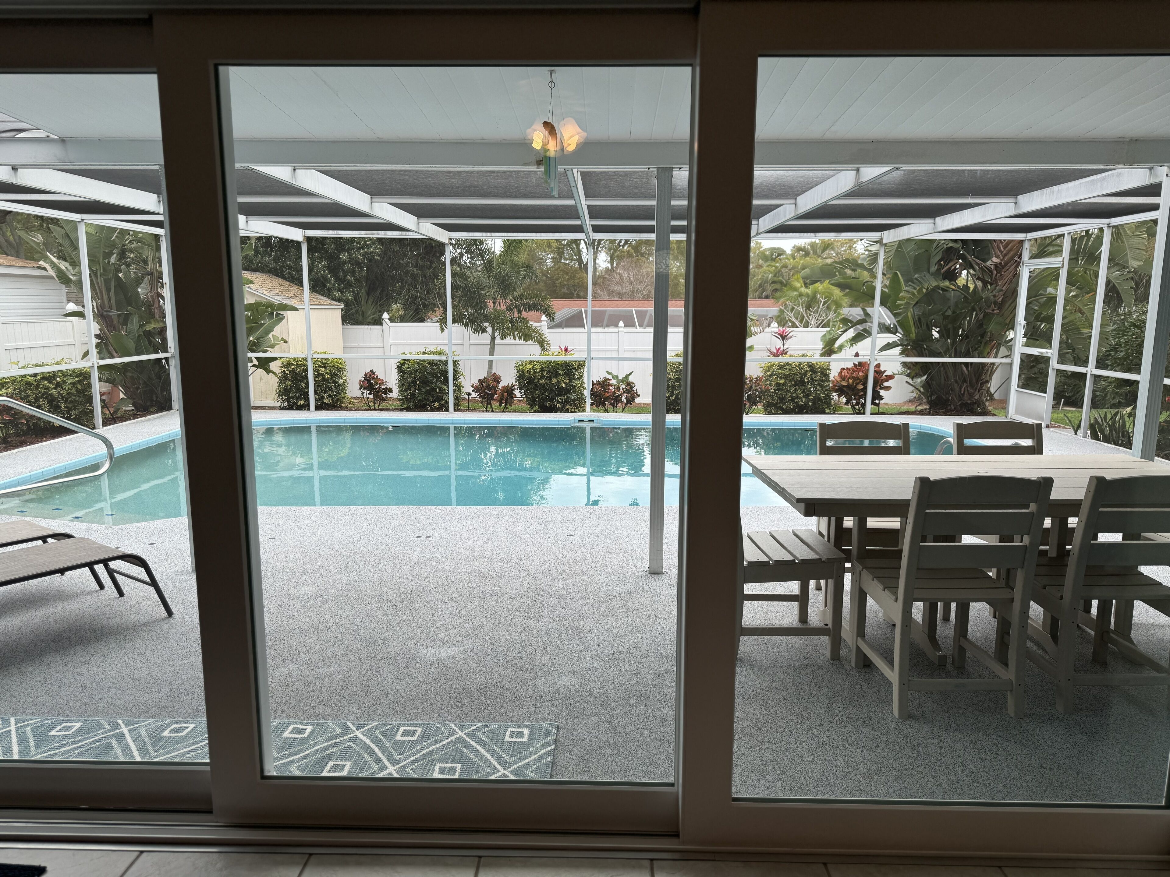 A pool area with a covered patio, a table, and chairs.