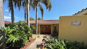 Una propiedad residencial con camino de entrada pavimentado, palmeras y una puerta roja.