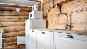 Une cuisine de taille réduite avec des murs en bois, un réfrigérateur blanc, un four à micro-ondes, un évier avec un robinet et une horloge au mur.