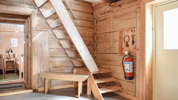 L’intérieur d’une cabane en bois, avec un escalier en bois, un extincteur et une porte.