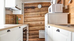 Une cuisine compacte aux murs en bois, avec des meubles blancs, un four encastré, un four à micro-ondes et un petit réfrigérateur.