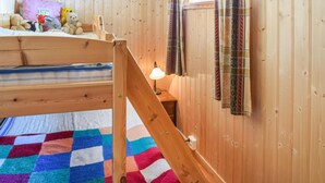 Uma cama beliche de madeira com um edredom colorido, uma luminária de cabeceira e uma pequena prateleira com brinquedos de pelúcia.
