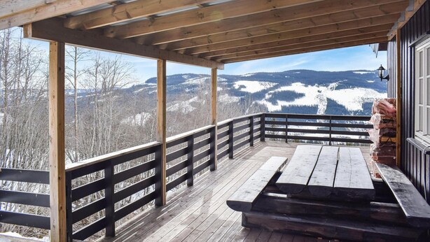 Um deck de madeira com um banco e guarda-corpo de madeira, com vista para uma paisagem montanhosa coberta de neve.