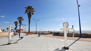 Un espace extérieur aménagé pour faire de l’exercice, avec des vélos d’appartement et des bancs, des palmiers et une vue dégagée sur la mer.