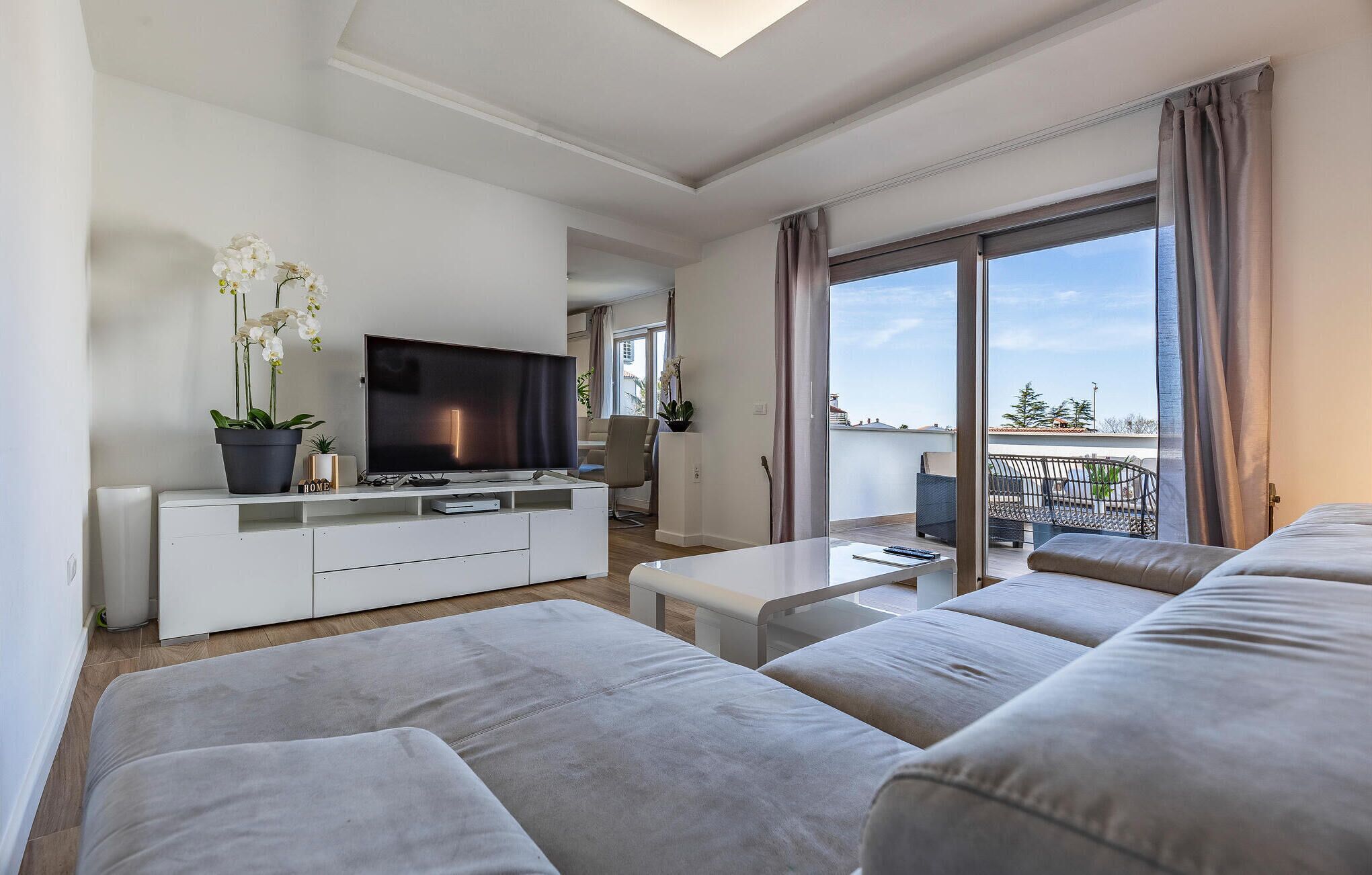 Una sala de estar moderna con un televisor de pantalla plana, un sofá, una mesa de centro y un balcón con vistas.