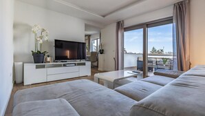 Ein modernes Wohnzimmer mit Flachbildfernseher, einer Couch, einem Couchtisch und einem Balkon mit Blick.