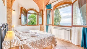 A bedroom with a large bed, a lamp, a radiator, and multiple windows with curtains. - 6 bedroom nice home in Montaione (Montaione)