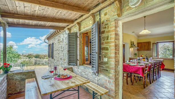 A rustic dining area with a wooden table set for two, a stone wall, and a view of the countryside. - 6 bedroom nice home in Montaione (Montaione)