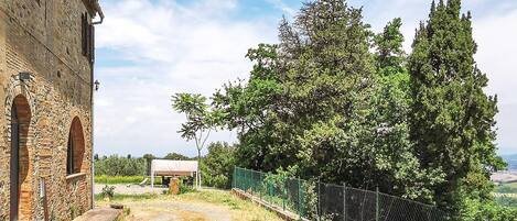 Un edificio de piedra con ventanas arqueadas, un sendero de tierra y un área cercada con árboles.