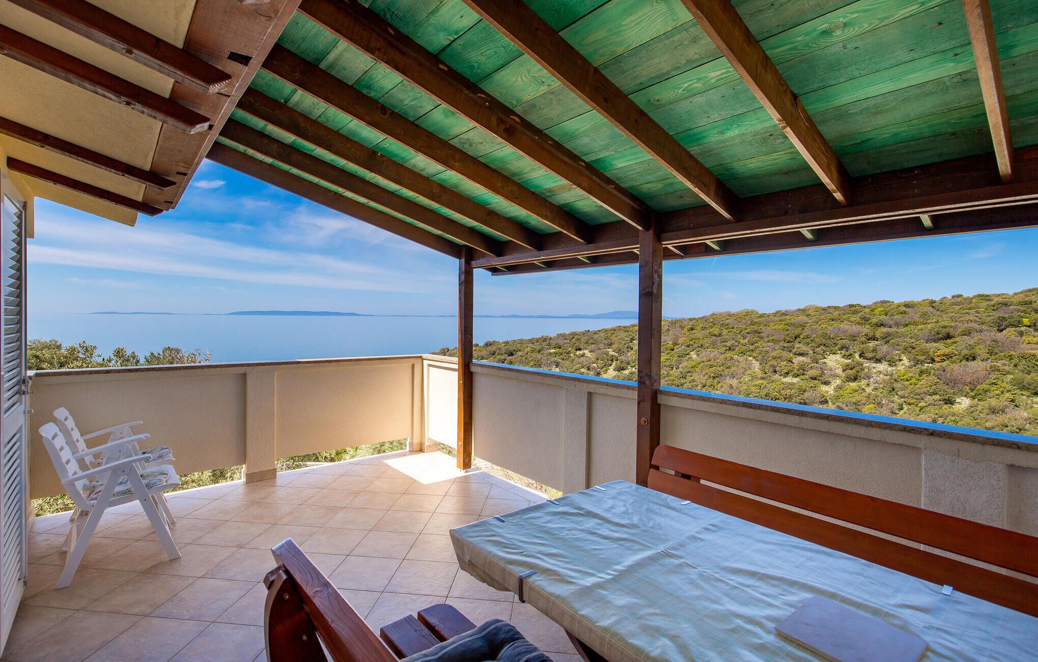 Ein Balkon mit einem Bett, einem Sessel und Blick auf das Meer und die Hügel.