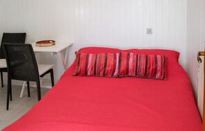 A room with a bed, a chair, a small table, and a wall socket.
